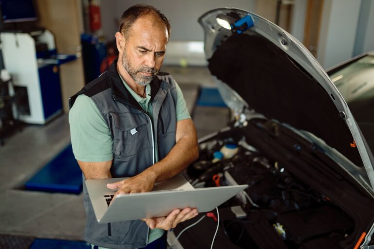 garagiste effectuant le contrôle technique complet d'une auto à l'aide de son logiciel professionnel sur ordinateur portable